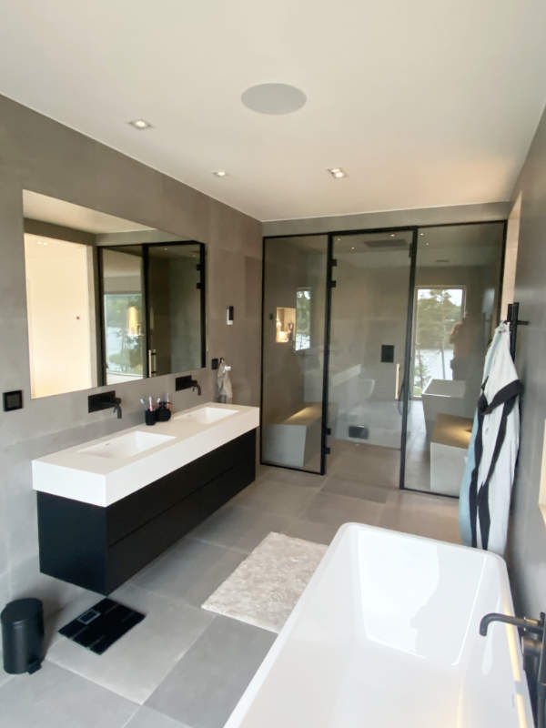 Modern bastu med glasvägg och svart ram i ett lyxigt, grått badrum.