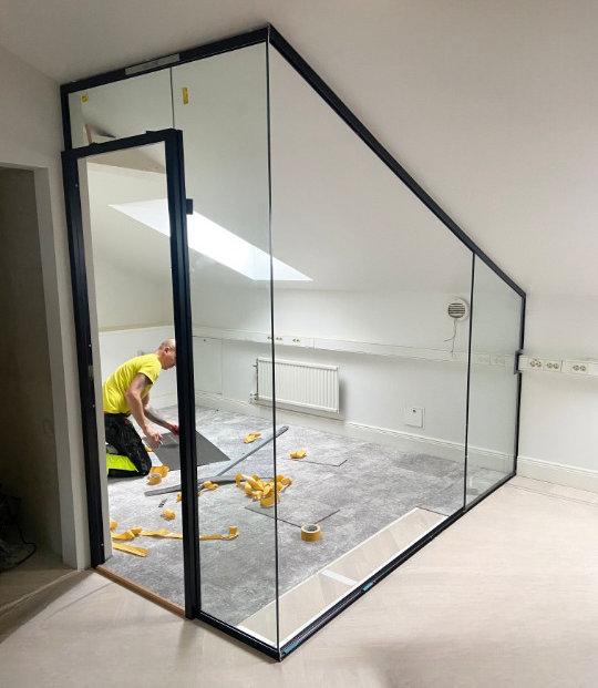 Installation av en glasvägg med svart ram i ett vindsrum av en hantverkare.