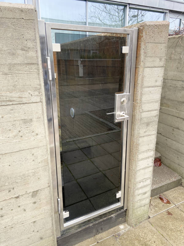 En glasdörr i rostfritt stål, monterad i en öppning mellan två betongväggar utomhus.