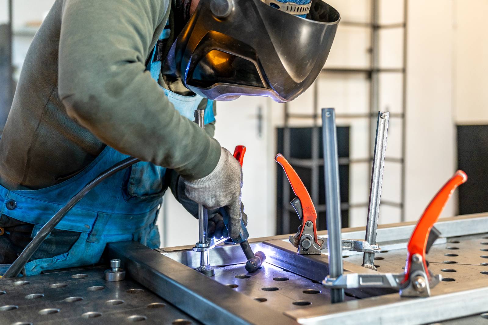 En smed i skyddsutrustning svetsar en metallkonstruktion på ett arbetsbord.